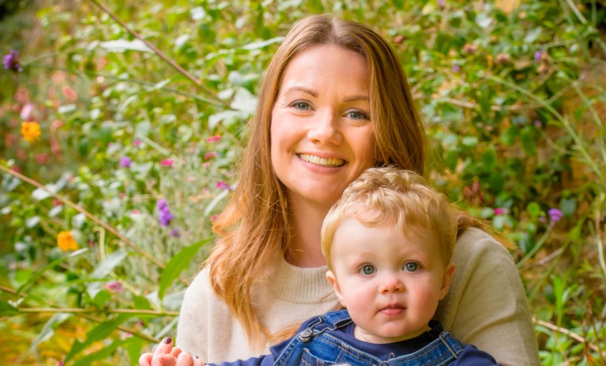 Rebecca Blake and her son on her lap outside with flowers in the background