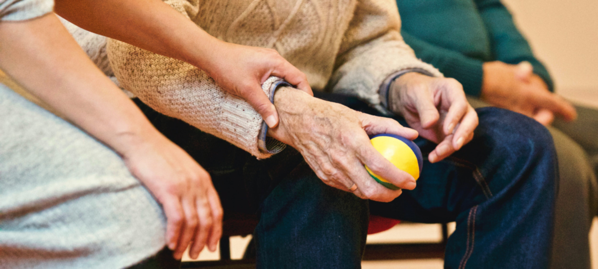 Older man holds a ball as a person checks he is okay