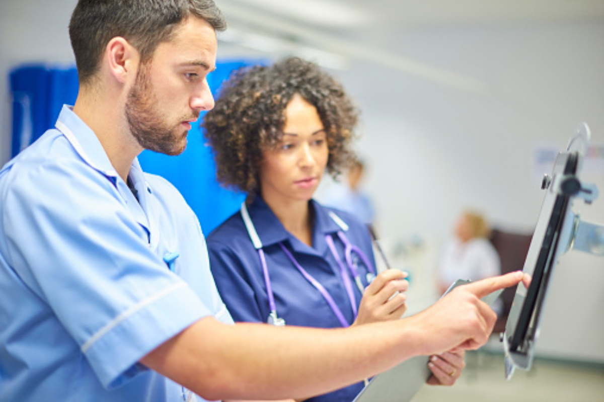 Male nurse and female doctor looking at a computer screen on a hospital ward