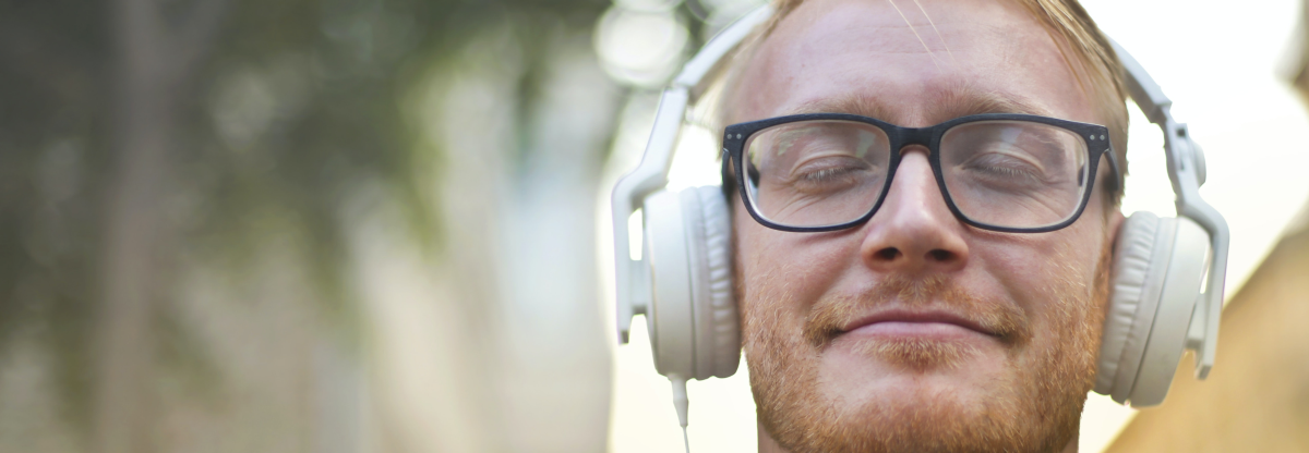 A man smiles with his eyes closed as he listens to music through headphones