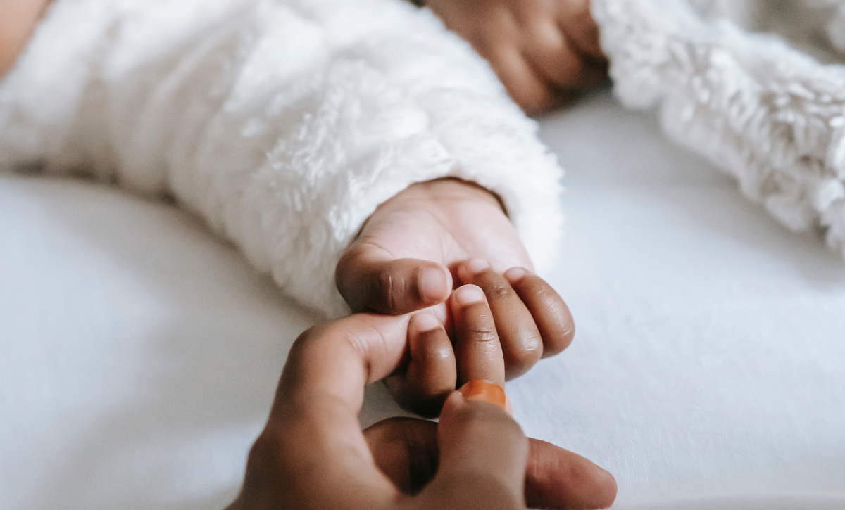 An adult holds a baby's hand.