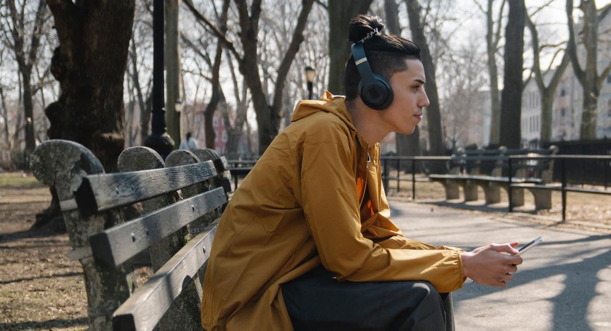 A man listens to music through headphones on a park bench