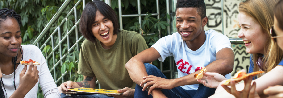 Teenagers laugh whilst eating pizza