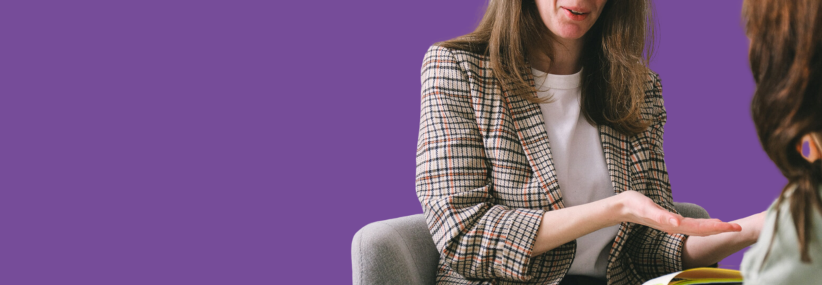 A close-up photograph of a mental health professional in a therapy session with a patient against a purple background