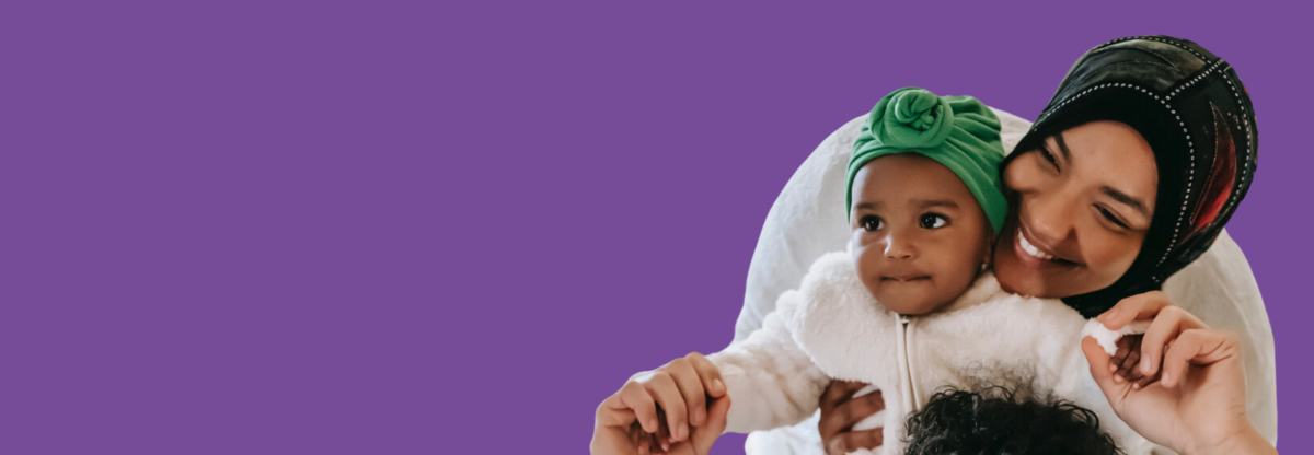A mum holding a baby and smiling against a purple background