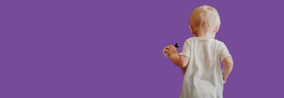 A toddler holding a toy viewed from behind against a purple background