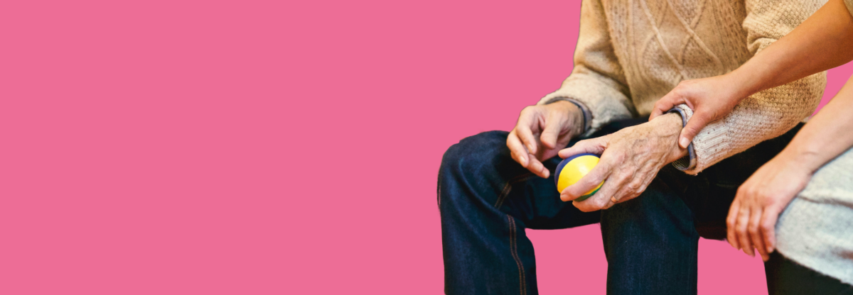 Man holding a ball with a nurse helping him against a pink background
