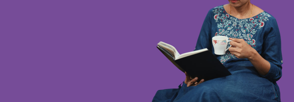 A photograph of an unidentified woman reading a book while holding a mug against a purple background