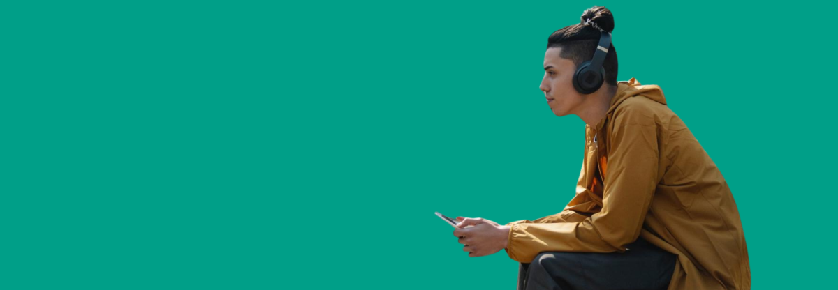 A man listens to music through headphones on a park bench against a green background