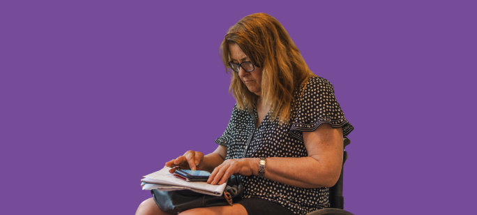 A cutout photograph of an older woman in a wheelchair looking at a mobile phone in her lap on top of documents